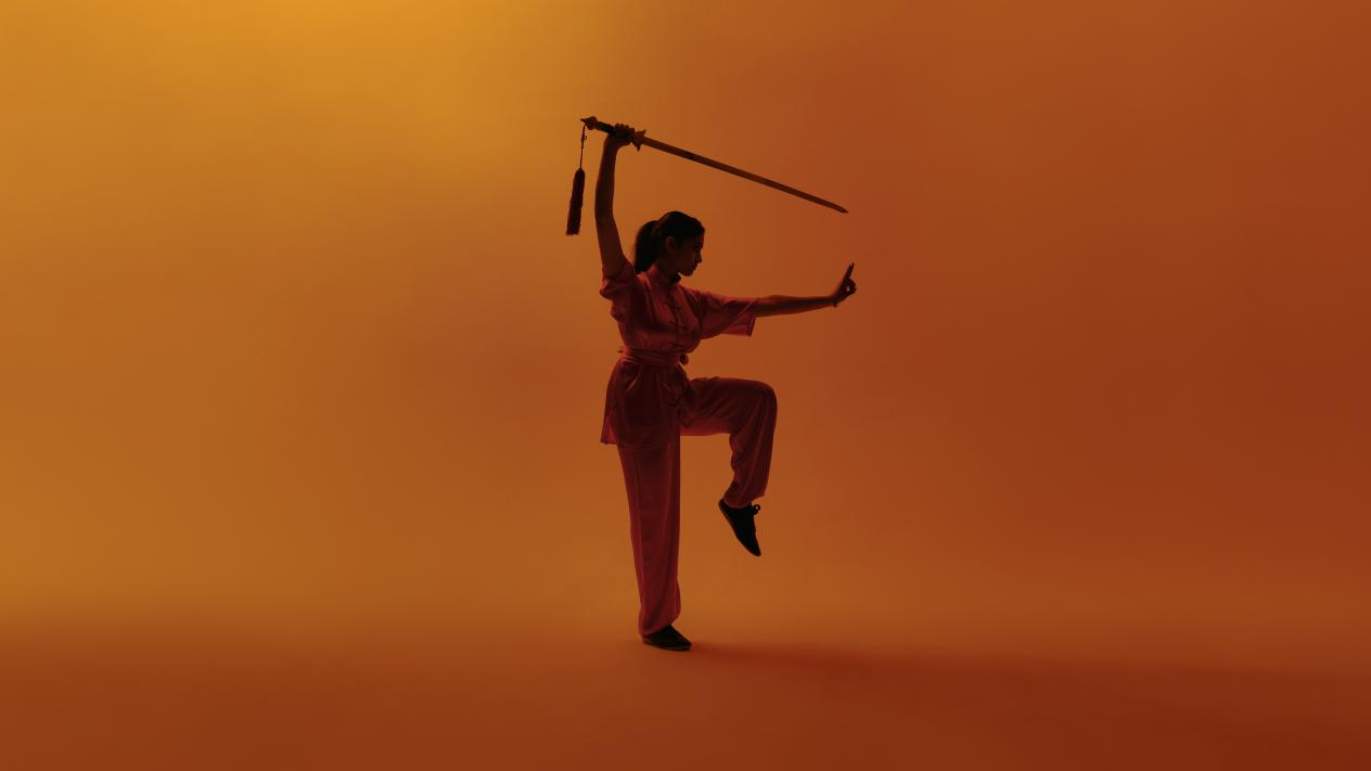 Wushu pose met zwaard op oranje achtergrond