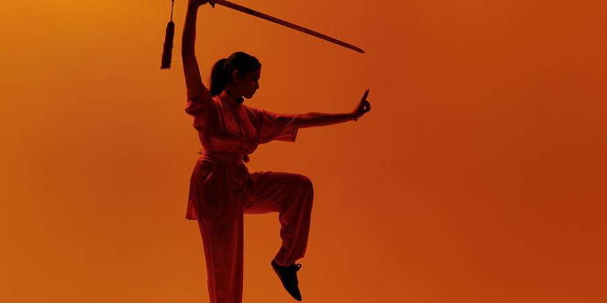 Wushu pose met zwaard op oranje achtergrond