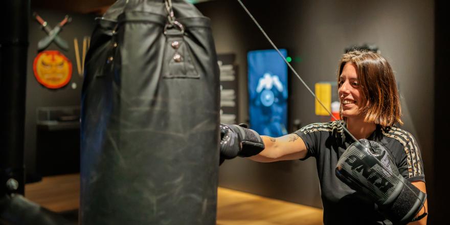 Glimlachende vrouw bokst tegen een zwarte bokszak. 