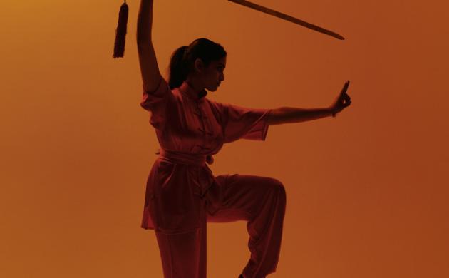 Wushu pose met zwaard op oranje achtergrond