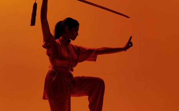 Wushu pose met zwaard op oranje achtergrond