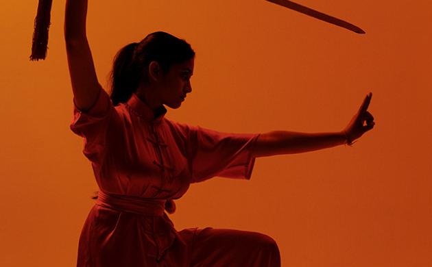Wushu pose met zwaard op oranje achtergrond