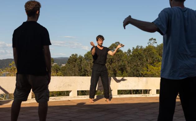 Olivier Goetgeluck geeft workshop. Hij staat centraal tussen twee deelnemers. De coach toont een beweging met open armen.