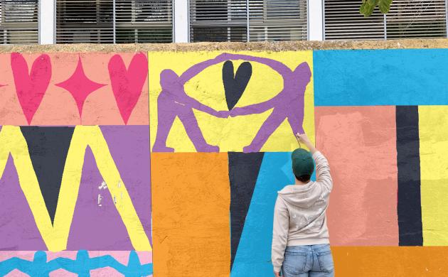 Persoon werkt aan kleurrijke muurschildering over queer verbondenheid