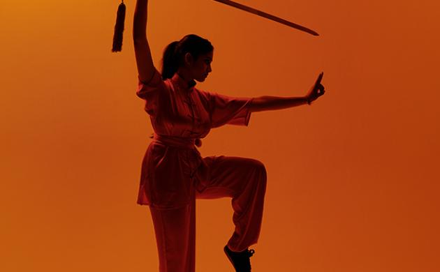 Wushu pose met zwaard op oranje achtergrond