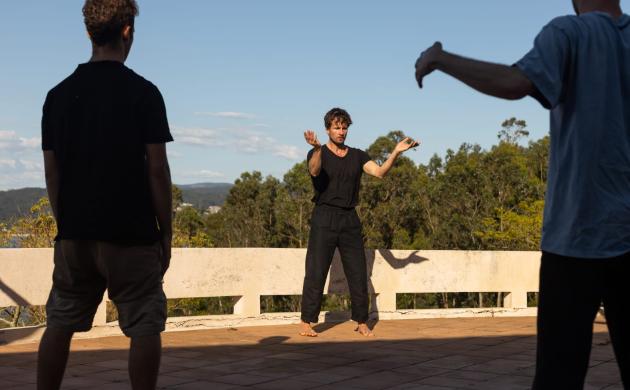 Olivier Goetgeluck geeft workshop. Hij staat centraal tussen twee deelnemers. De coach toont een beweging met open armen.