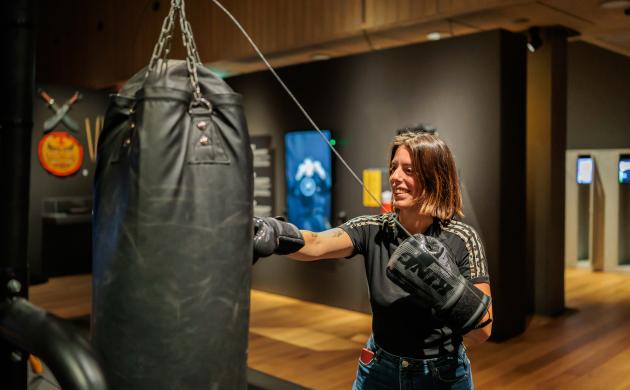 Glimlachende vrouw bokst tegen een zwarte bokszak. 