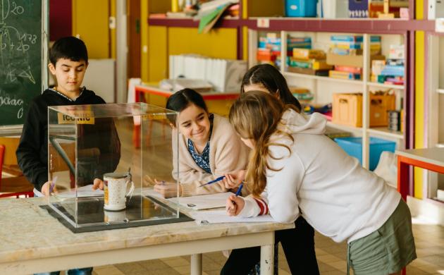 Schrijfdag De Wondere Pluim kinderen staan rond een tafel met een object in een vitrine