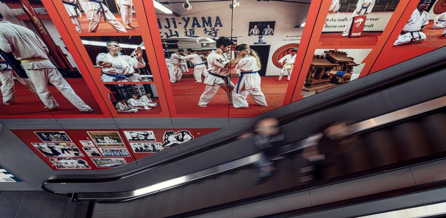 Fotowand met karatebeelden langs een roltrap.