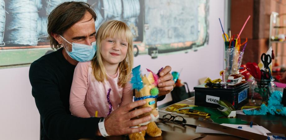 man met kind op de schoot aan een tafel met knutselmateriaal