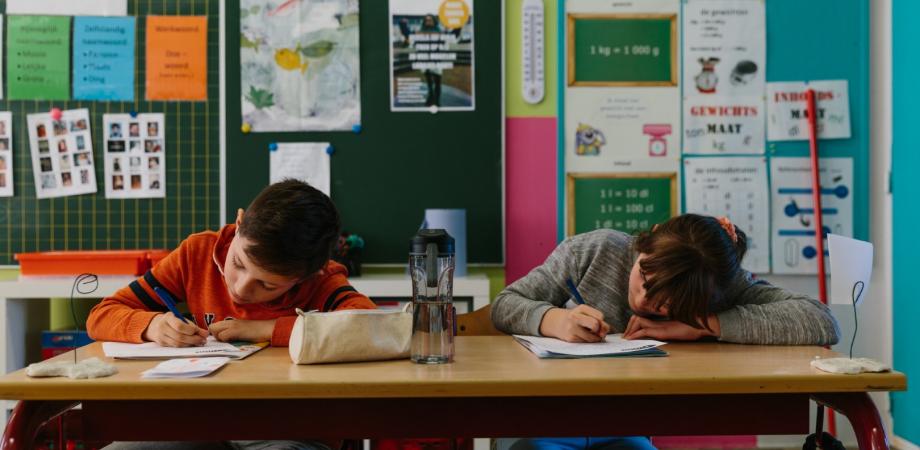 2 kinderen zitten aan een schoolbank en schrijven