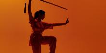 Wushu pose met zwaard op oranje achtergrond