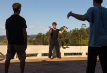 Olivier Goetgeluck geeft workshop. Hij staat centraal tussen twee deelnemers. De coach toont een beweging met open armen.